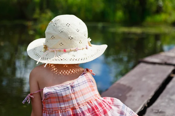 Urocza mała dziewczynka siedzi na drewniany most i starannie patrząc na rzece — Zdjęcie stockowe