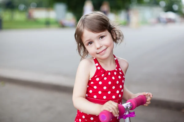 Portrait of cute toddler girl in red dress on the scooter — Stock Photo, Image