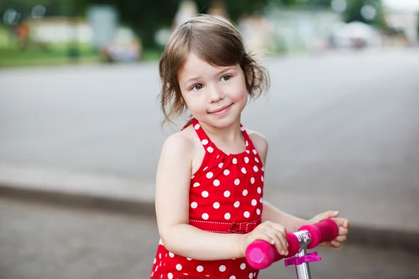 stock image Portrait of cute toddler girl in red dress on the scooter