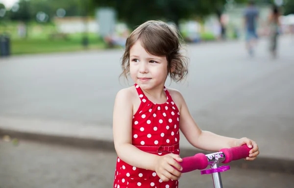 stock image Portrait of cute toddler girl in red dress on the scooter