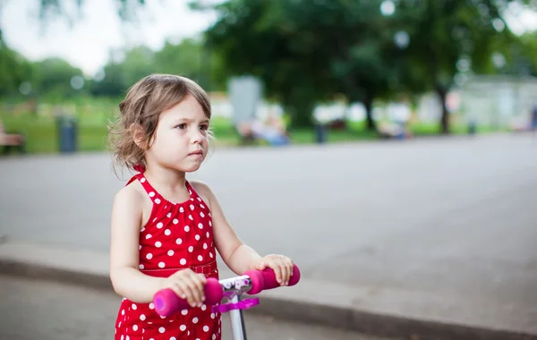 Stock image Portrait of cute toddler girl in red dress on the scooter