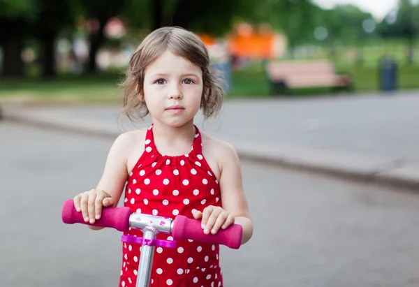 stock image Portrait of cute toddler girl in red dress on the scooter