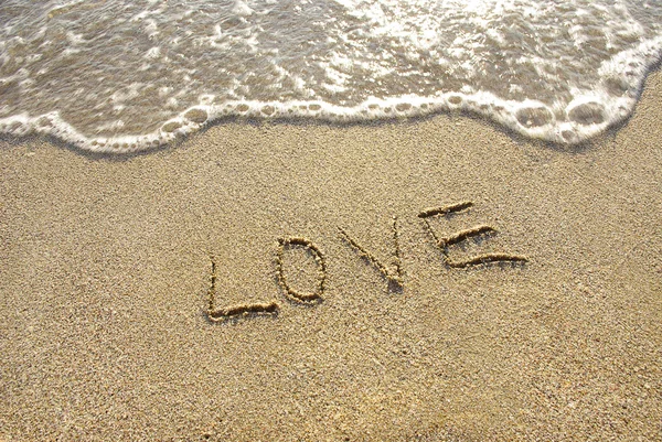 Любов намальована в піску з морем і хвилею — стокове фото