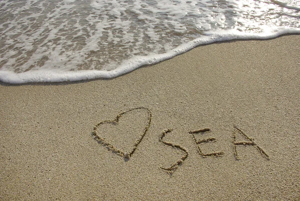 Heart drawn in the sand with seafoam and wave — Stock Photo, Image