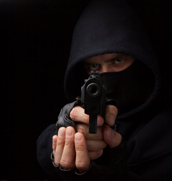 Masked robber with gun aiming into the camera