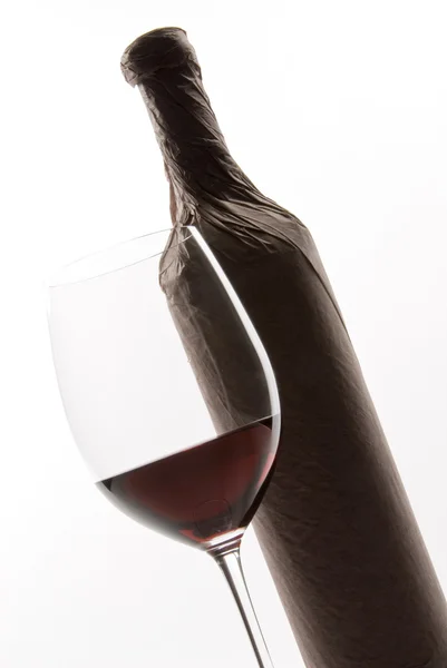 Copo de vinho tinto ao lado de uma garrafa embrulhada com papel — Fotografia de Stock