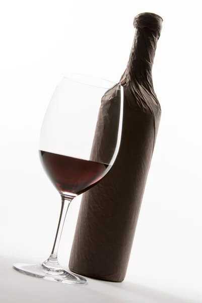 Glas rode wijn naast een fles omwikkeld met papier — Stockfoto