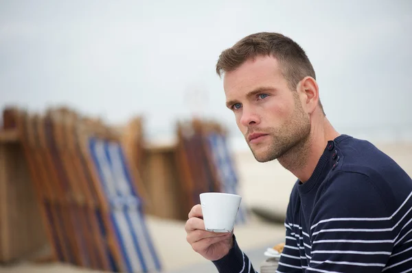 Fiatal ember iszik a kávé a strandon — Stock Fotó