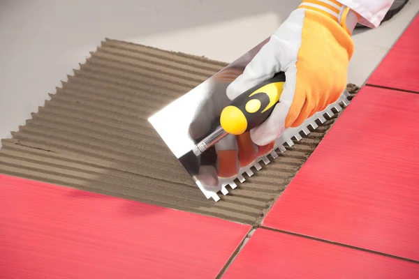Работник с зубчатой лопаткой устанавливает красную плитку с клеем — стоковое фото