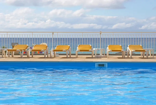 Șezlonguri la piscină în jurul unei piscine cu mare în fundal — Fotografie, imagine de stoc