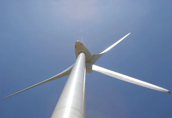 Up perspective of wind mill power generator against blue sky with lens flare — Stock Photo, Image