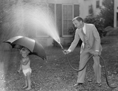 Toddler and dad playing with hose in yard clipart