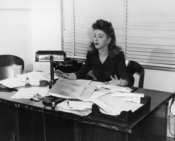 ペーパーで覆われた机で働く女性 — ストック写真