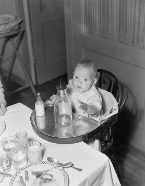 Baby in hoge stoel met grote en kleine flessen — Stockfoto