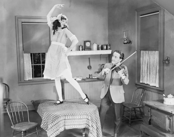 Мужчина играет на скрипке для женщины, танцующей на столе — стоковое фото