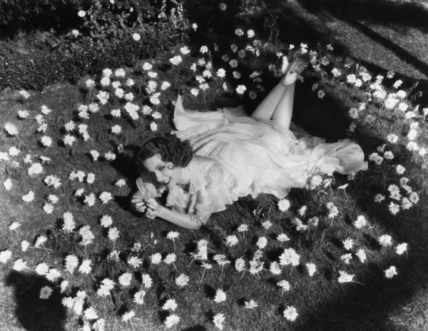 Kvinna liggande på gräs som omges av blommor — Stockfoto