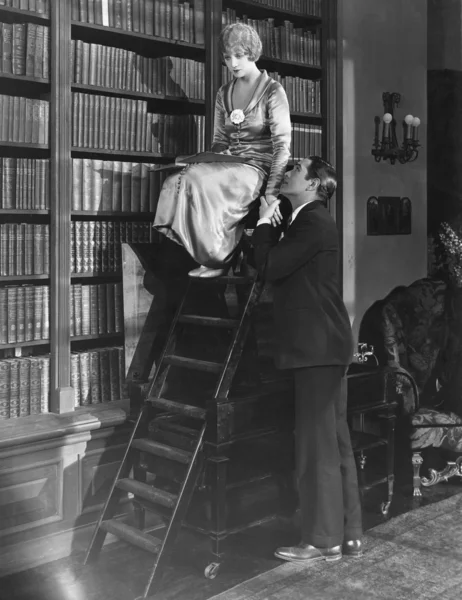 Man with woman on ladder in library — Stock Photo, Image