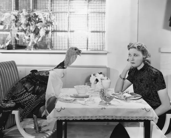 Frau isst Essen am Tisch mit lebendem Truthahn Stockbild