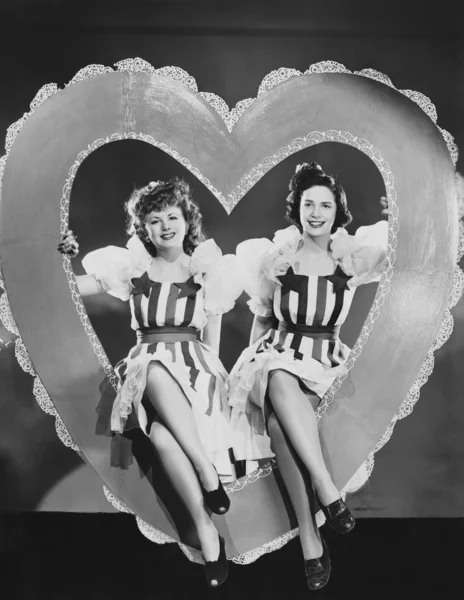 Portrait of two women sitting in large heart Stock Picture