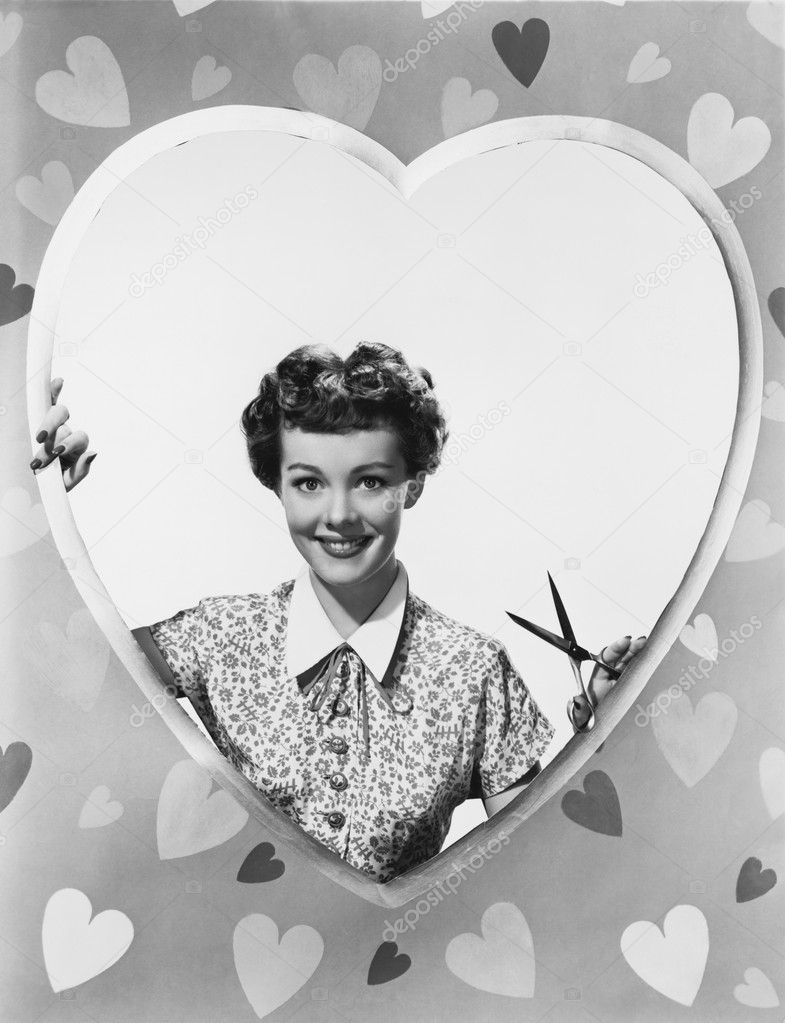 Woman looking through heart shape with scissors