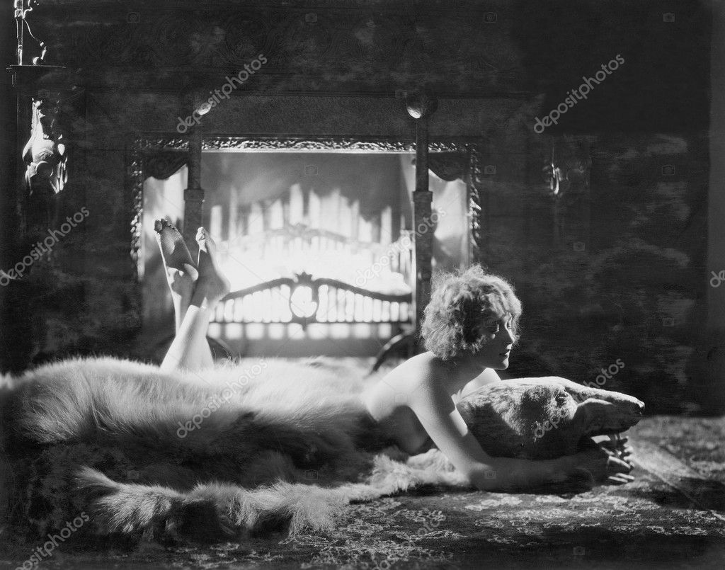 Woman relaxing on bear rug in front of fire - Stock Photo, Image. 