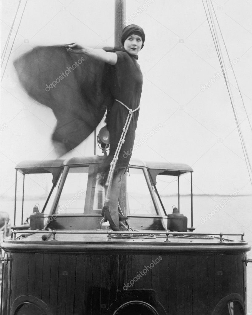 Woman standing on boat with cape fluttering in wind