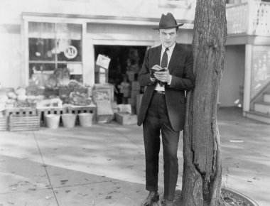 Detective leaning against tree taking notes clipart