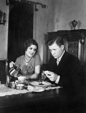 Glum man and adoring woman at breakfast table clipart