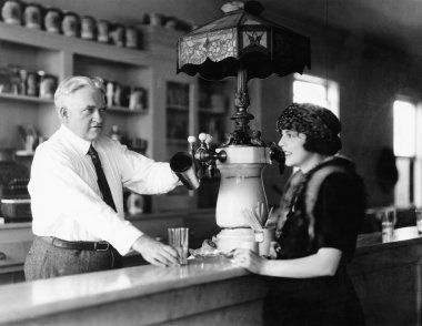 Man serving beverage to woman at counter clipart