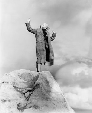 Woman atop rock on windy day clipart