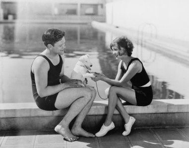 Couple sitting with their puppy next to a pool clipart