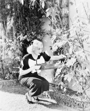 Young woman with a big saw trying to cut flowers clipart