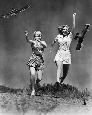 Two women running and playing with model airplanes clipart