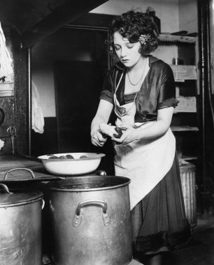 Woman in a kitchen peeling potatoes clipart