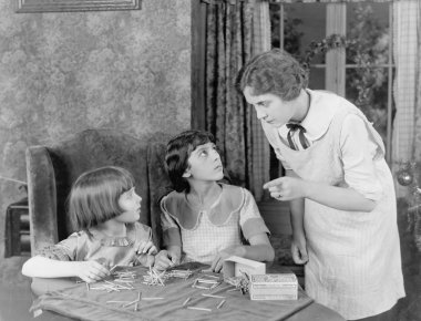 Woman scolding her two daughters for playing with matchsticks clipart