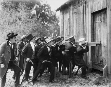 Group of men with guns and top hats breaking into a barn clipart