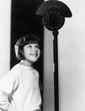 Profile of a young girl looking at a microphone and smiling clipart