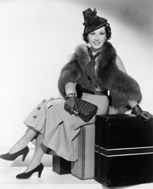 kadın bavul üzerinde oturan ve gülümseyen bir şapka ile