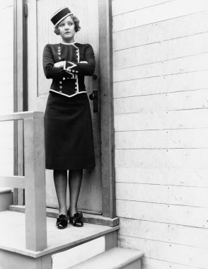 Young woman in a uniform standing with her arms crossed in front of a closed door clipart