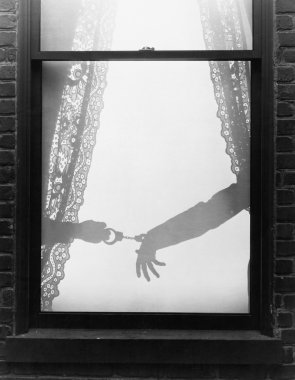 Silhouette of a hand arresting a person with handcuffs viewed through a window clipart