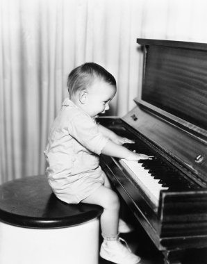 profili bir taburede oturan ve bir piyano çalan küçük bir çocuk