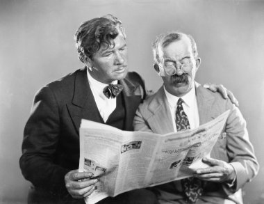 Two mature men reading a newspaper together clipart