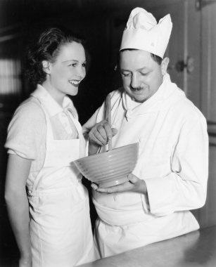 Profile of a chef stirring a mixture in a bowl and a young woman standing beside him clipart
