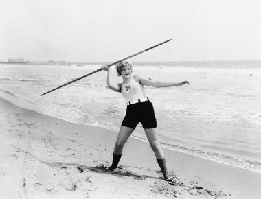 Young woman preparing to throw a javelin on the beach clipart