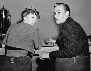 Portrait of a couple sitting on a counter and looking over their shoulders clipart