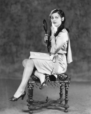 vanity ayna tutan bir taburede oturan genç kadın