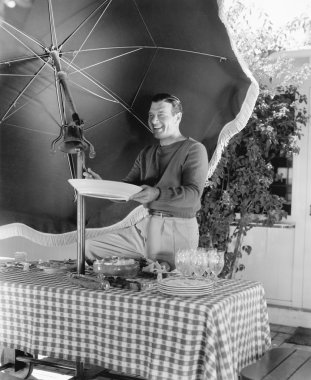 bir piknik masada duran ve bir tabak tutan adam