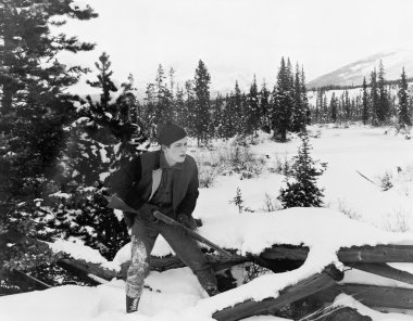 Hunter with his rifle walking through snow covered countryside clipart