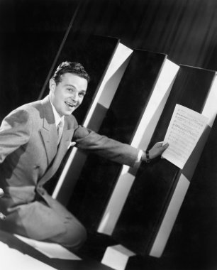 Man sitting with oversized books holding sheet music in his hands clipart