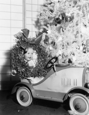 Little boy at Christmas sitting in his toy car clipart